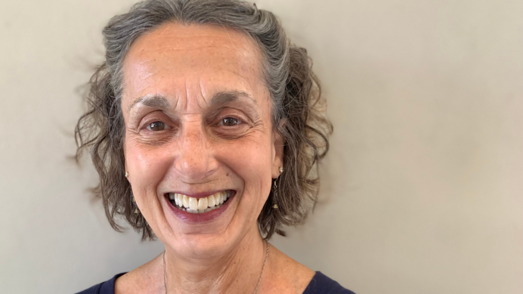 A woman smiles in front of a beige wall