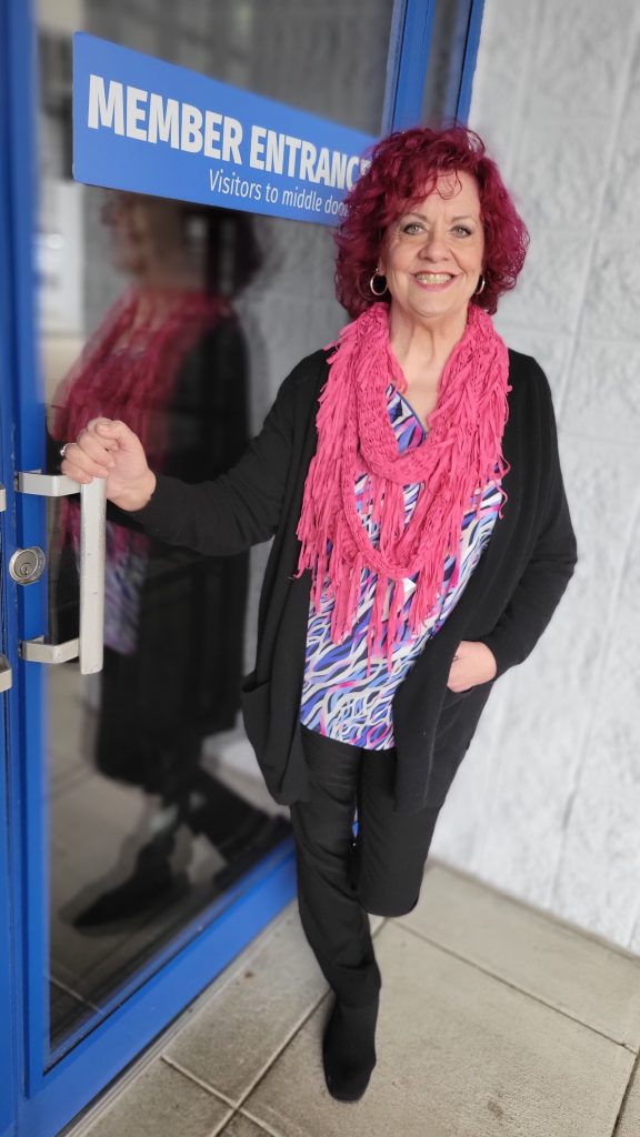 A woman in ruby-colored hair and brightly-colored scarf poses in front of The J's main entrance