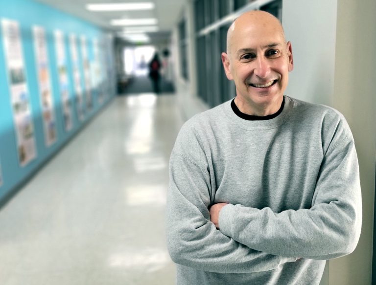 A man in a sweatshirt leans against the wall of a long hallway