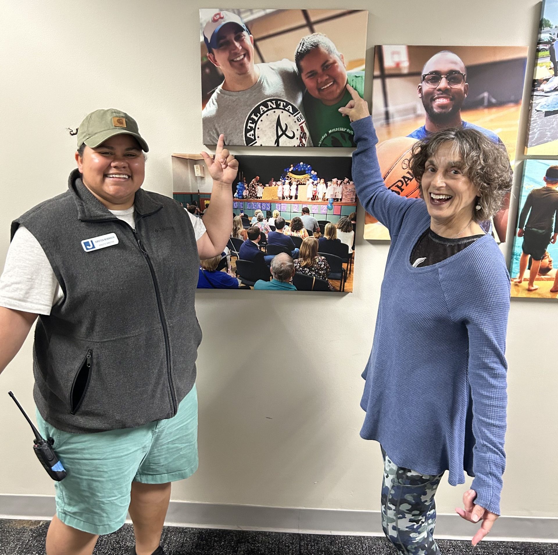 Two women stand in a hallway and together point to a picture on the wall