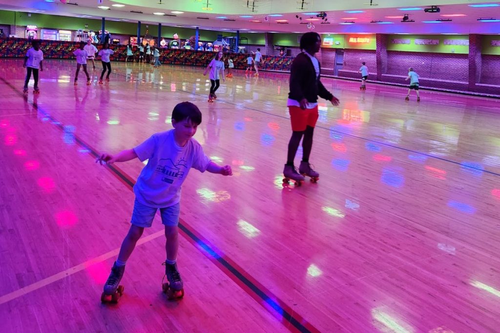 Kids rollerskate on a large indoor rink with violet lighting