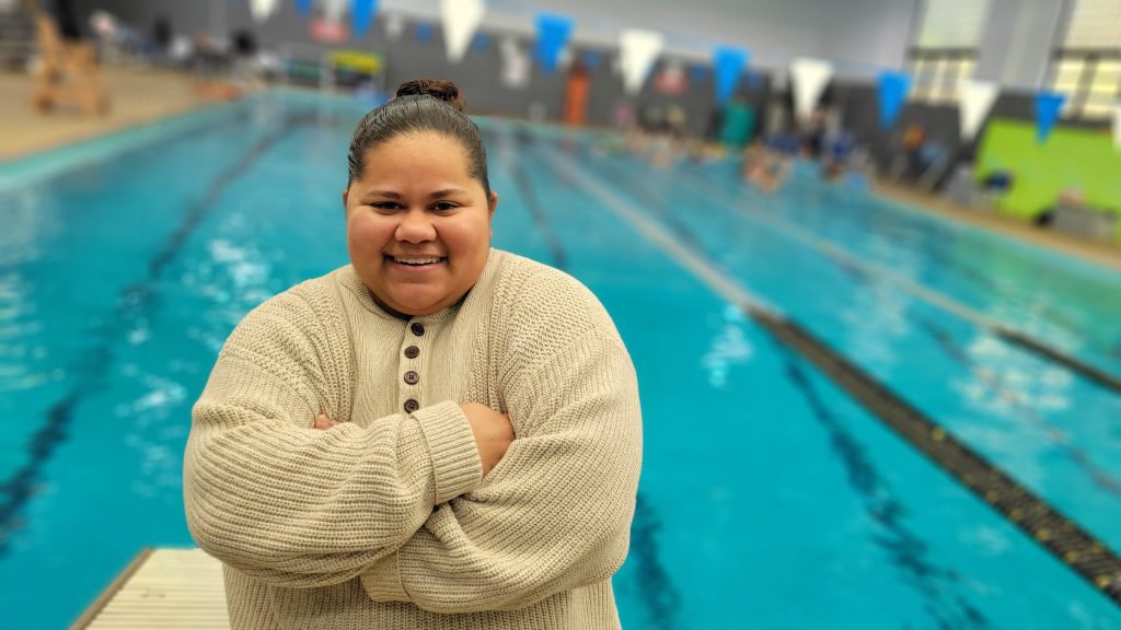 A woman in a sweater poses in front of an indoor pool