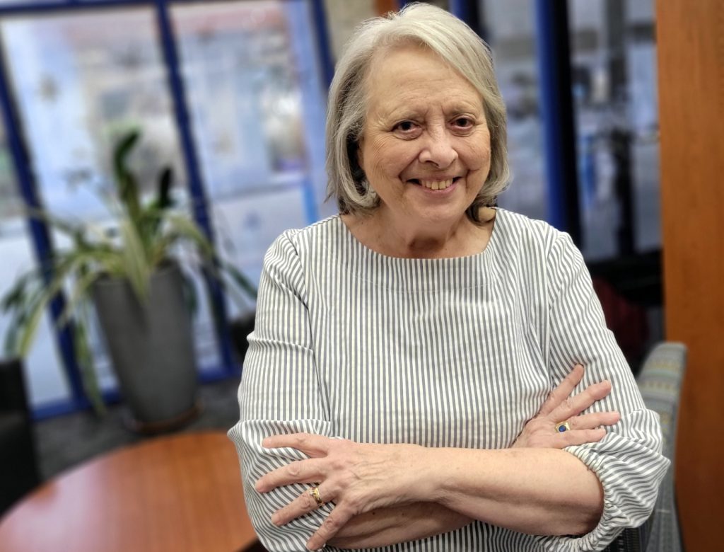An elderly woman poses with her arms crossed