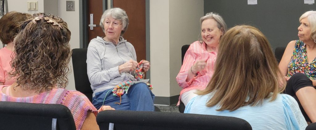 Six women seated in a circle are meeting up for The J's knitting group