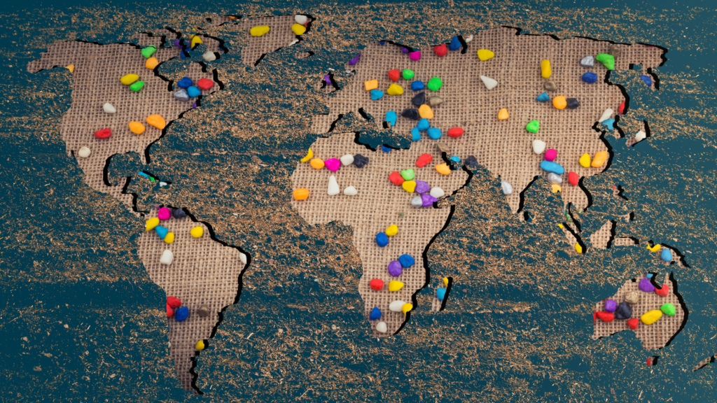 A world map crafted from burlap on wood and scattered with what looks like colorful bits of clay