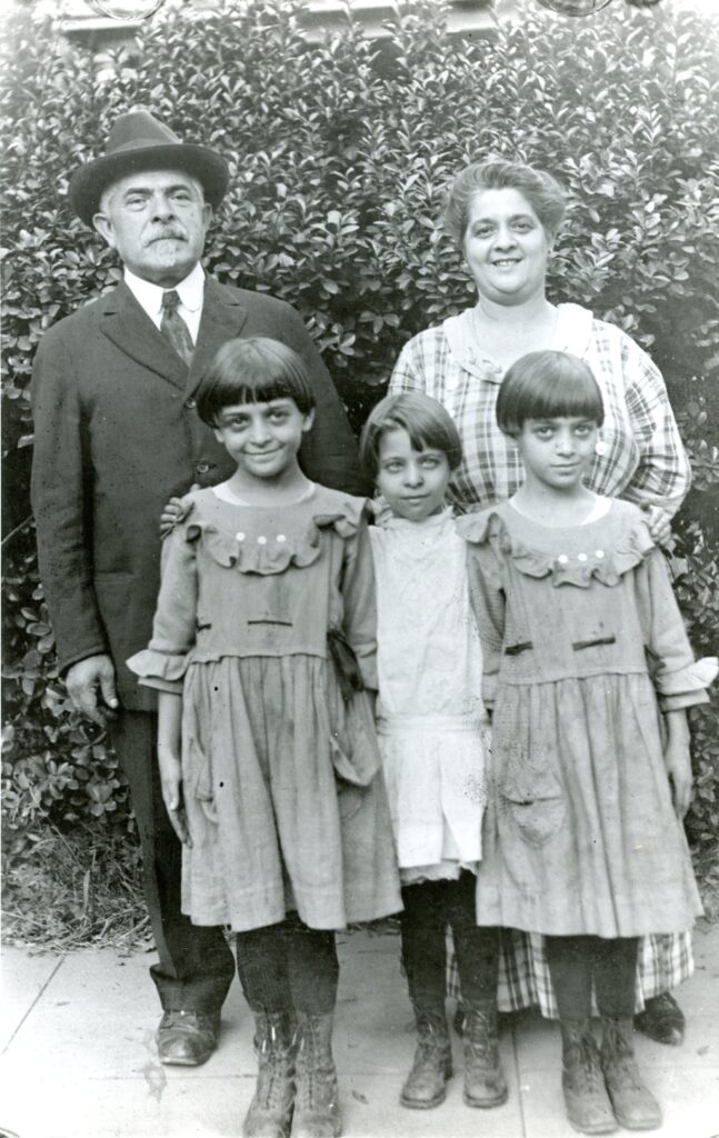 An old black and white photo showing a man in a bowler hat standing next to his wife with their three children lined up in front