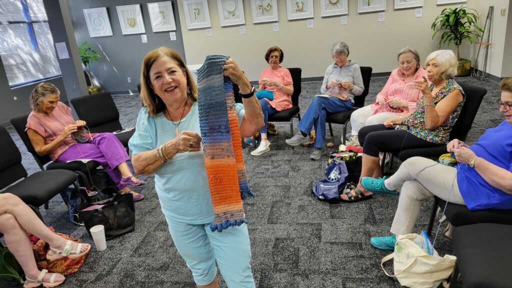 A woman holds a knit scarf she just finished as part of the knitting circle that meets weekly at The J