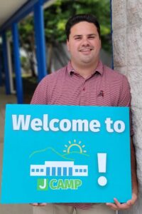 A man holds a "Welcome to J Camp" sign outside The J