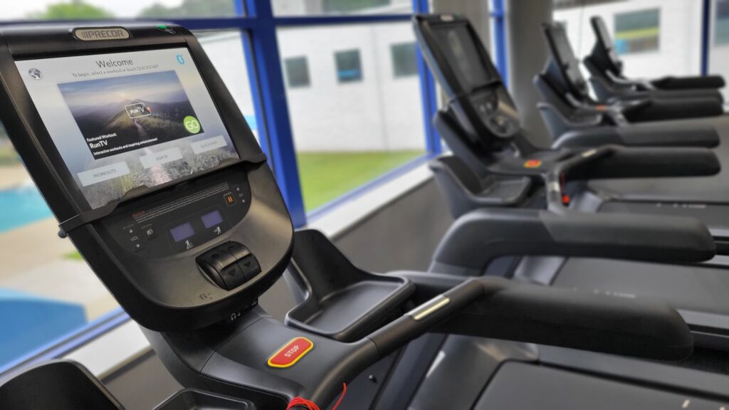 Five treadmills lined up next to each other in front of a large window
