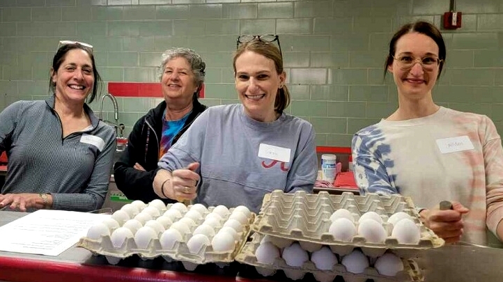 Four women in the kitchen pose behind containers full of eggs.