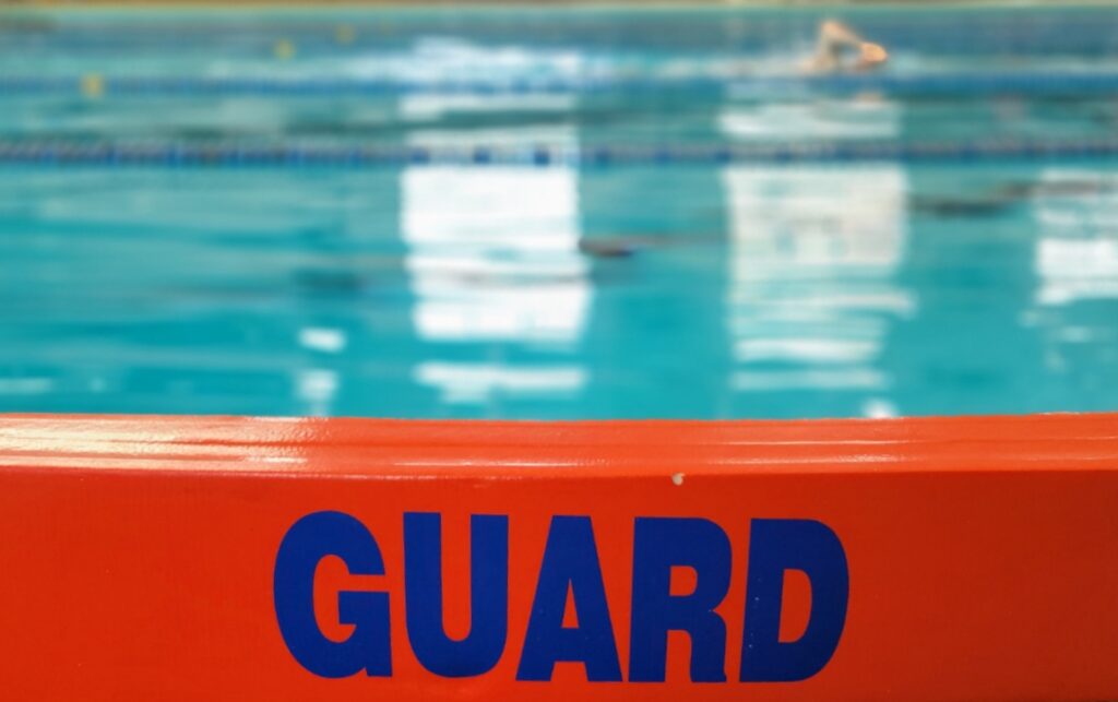 An orange foam bar lifesaving device with the word "guard" on it showing the indoor pool in the background