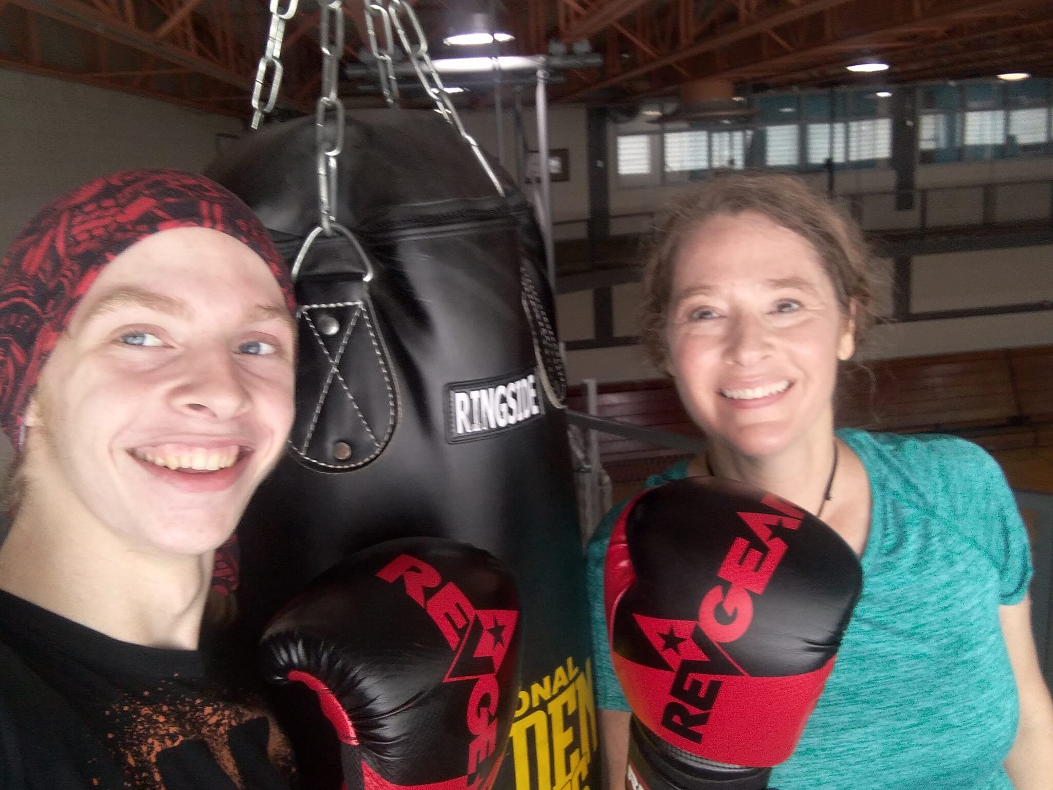 A woman and her son wearing boxing gloves flank a punching bag