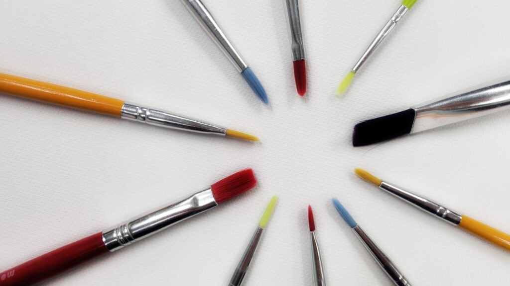 10 colored paint brushes are arrayed on a blank canvas with the brush tips forming the outline of a circle