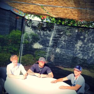 Three guys sit around a table in the sukkot they just finished building.