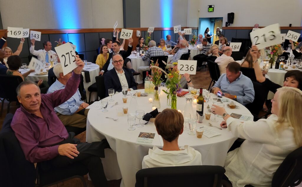 People sitting at a round table hold up their numbered auction cards in preparation for the live J'la Gala auction