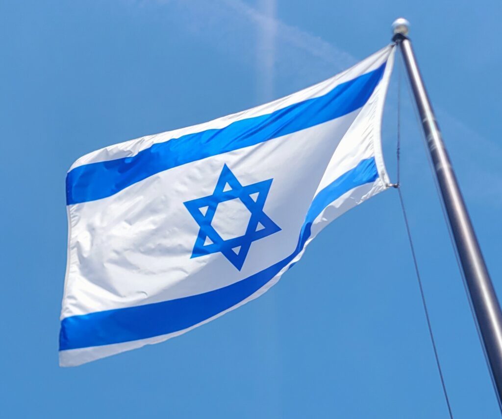An Israeli flag -- blue Star of David on a white field with blue bars top and bottom -- flutters in the breeze against a blue sky