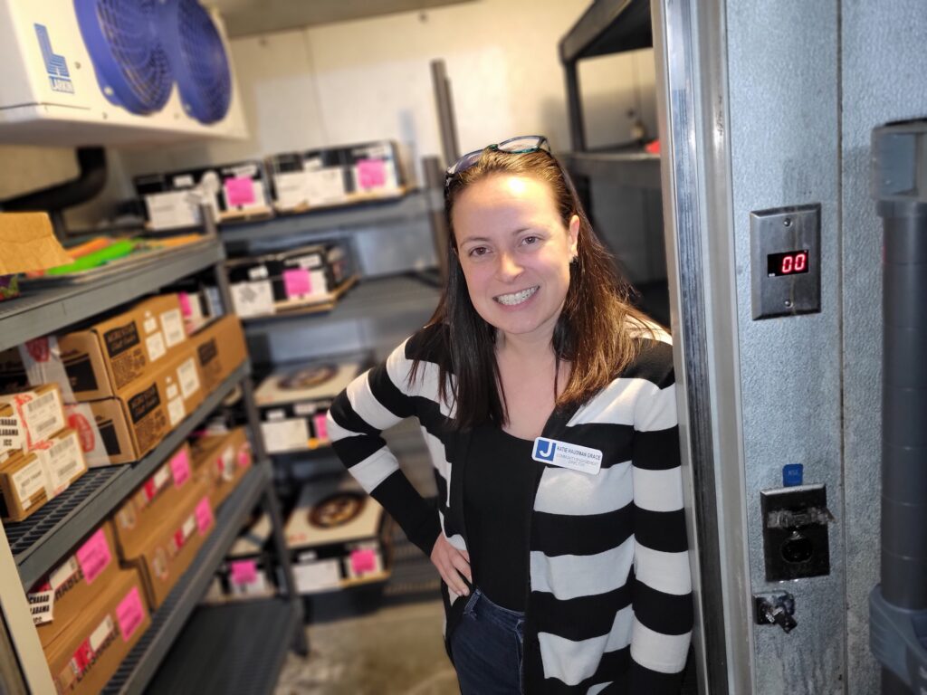 A woman in a black and white striped sweater smiles as she poses in the doorway of a walk-in freezer