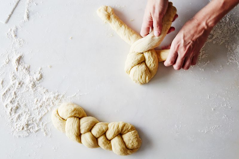 A stock image of someone making challah with a braided loaf before them