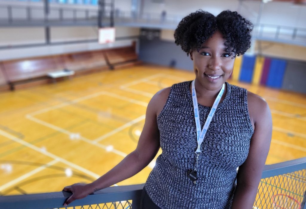 A woman poses at a railing overlooking a basketball court
