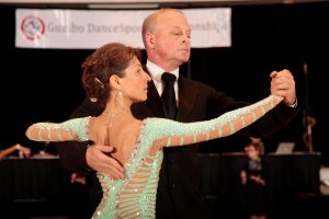 A man and a woman look elegant but serious as they hold a pose before starting a ballroom dance competition