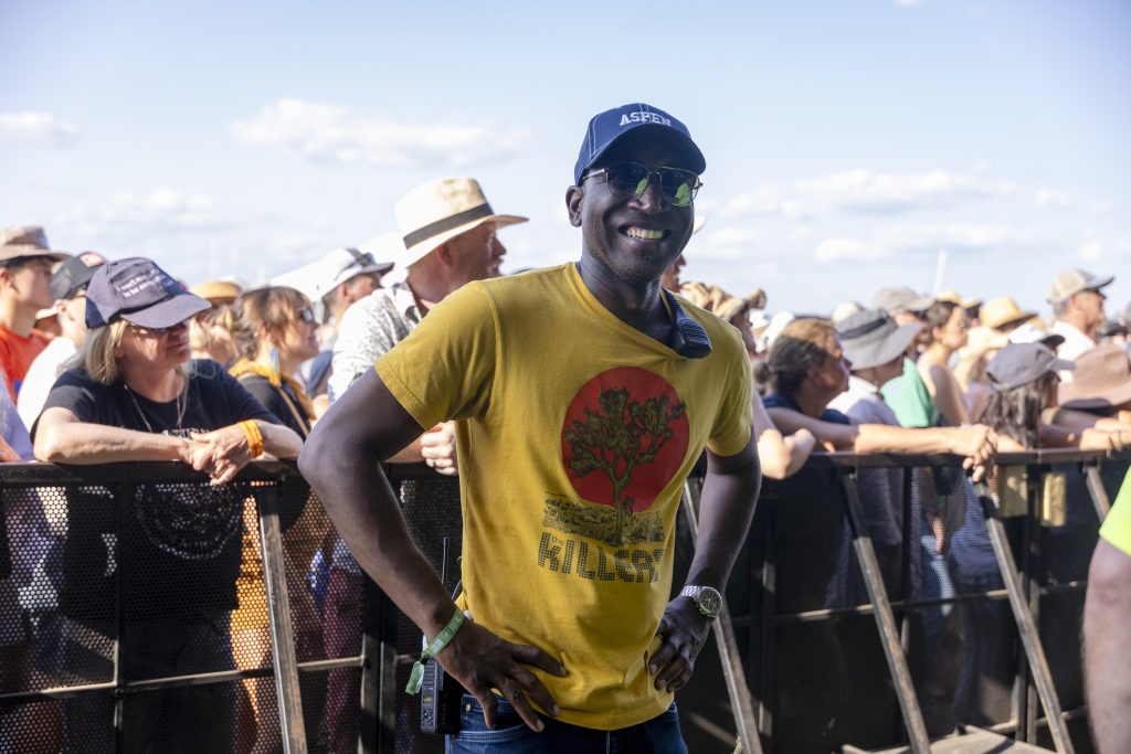 A man in a yellow shirt stands in front of a large outdoor concert crowd