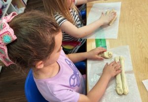 A young child shapes challah dough on a table