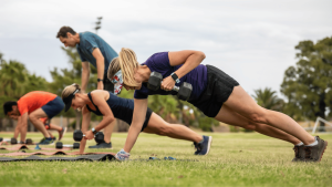 A group of people lift weights together outside on an athletic field