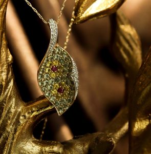A bejeweled pendant is suspended within a display of branches and leaves